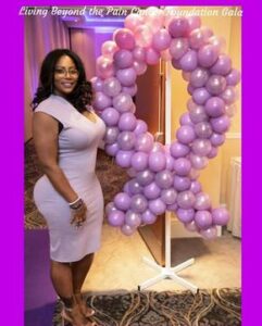 A woman standing next to balloons shaped like breast cancer awareness ribbon.