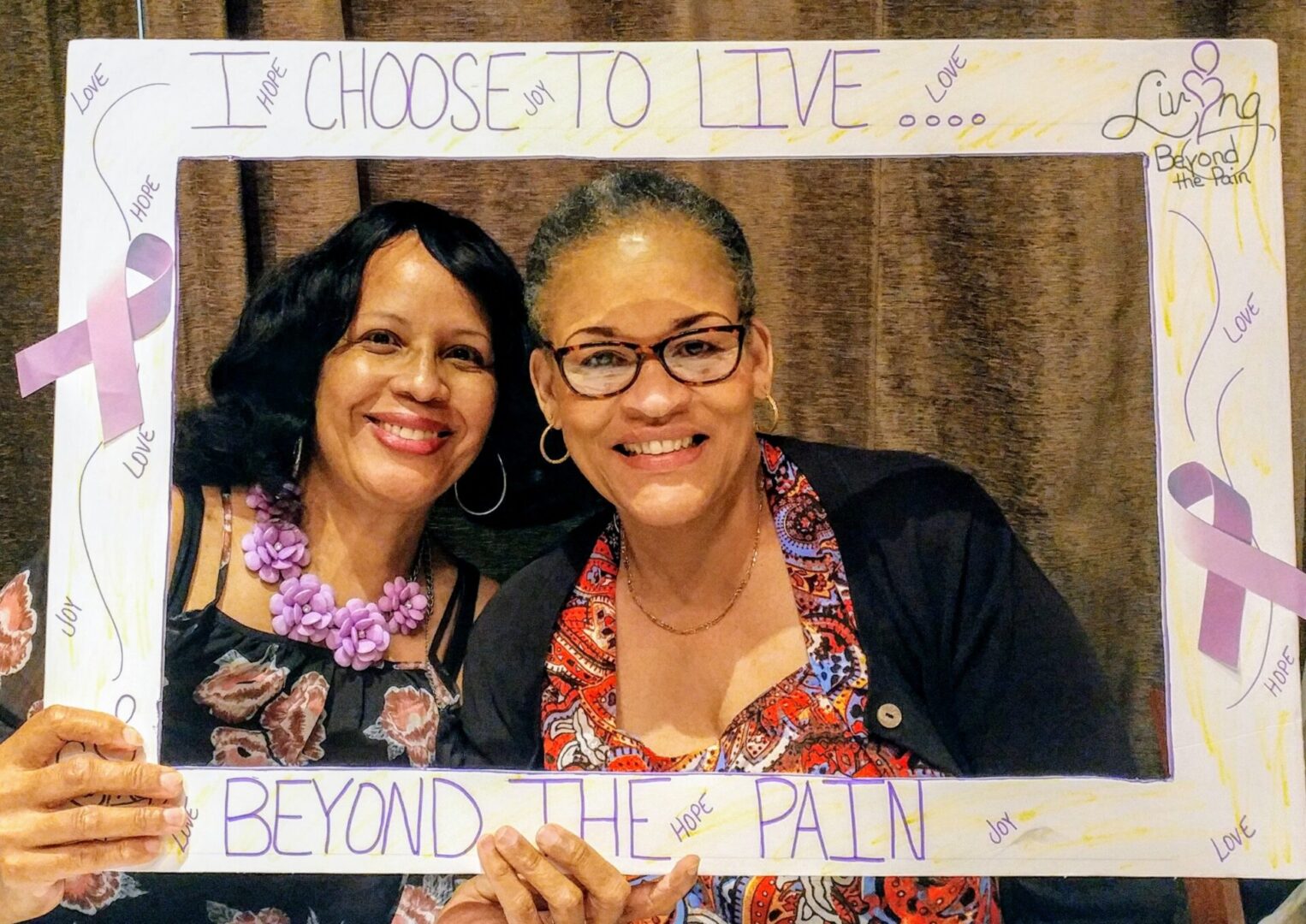 Two women holding signs that say i choose to live beyond the pain.