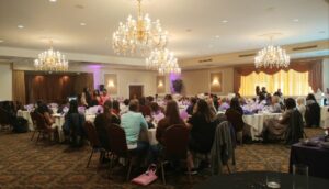 A group of people sitting at tables in front of chandeliers.